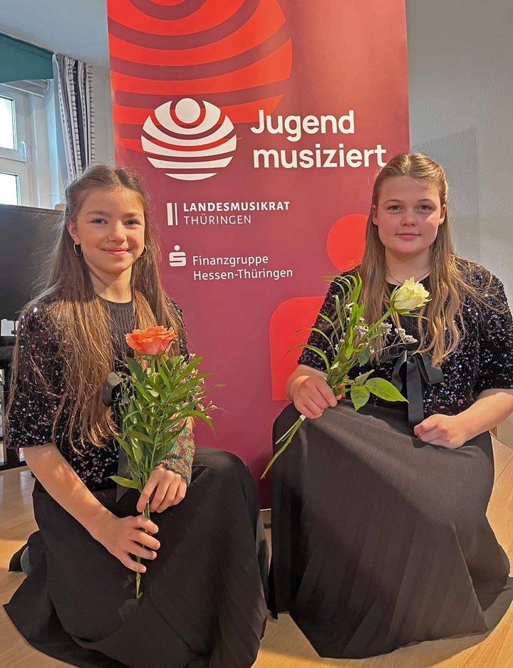 Hannah Ella Zaehle und Karla Schleenvoigt knieen mit einer Rose vor einem jugend musiziert Banner